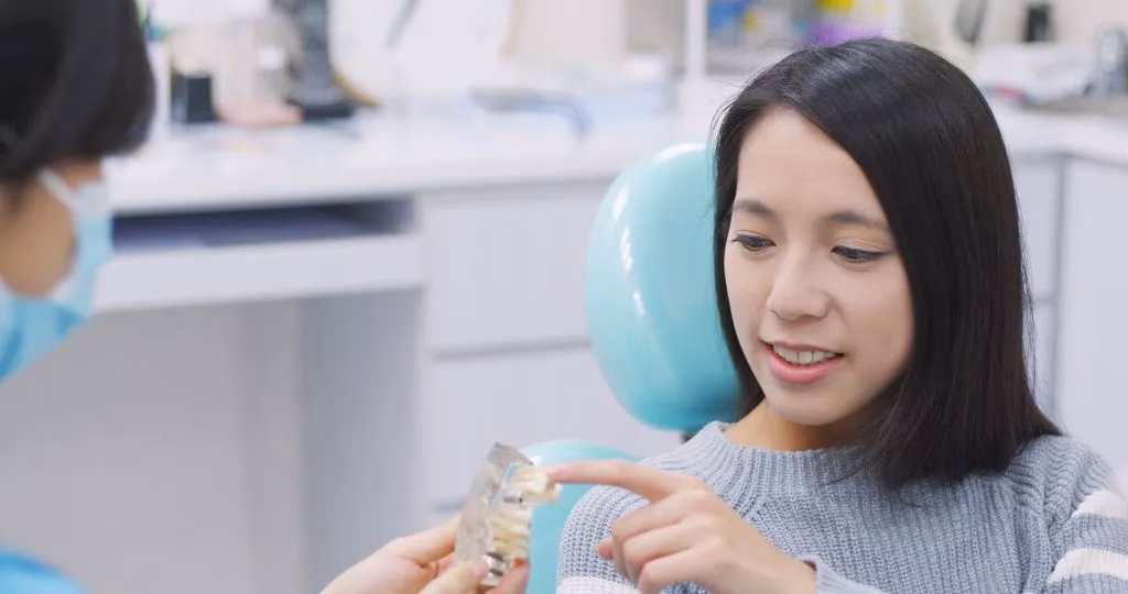 Dentist showing dental implant model to patient in modern dental office, emphasizing personalized care and advanced technology for implant procedures.