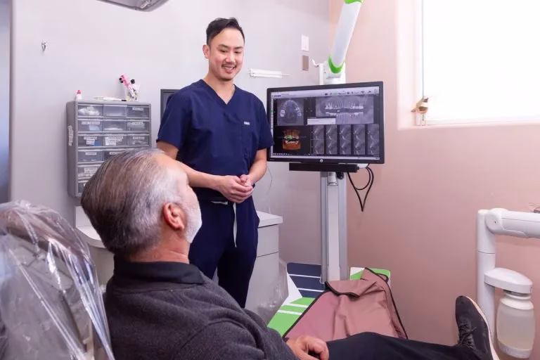 Dr. Le discussing dental implant treatment with a patient, featuring advanced imaging technology and a relaxing dental office environment.