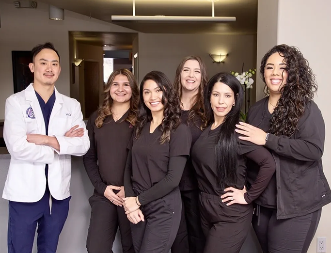 Dental team at Rosemary Dental Spa, featuring six professionals in black scrubs, including a male dentist in a white coat, smiling and posing in a modern office setting.