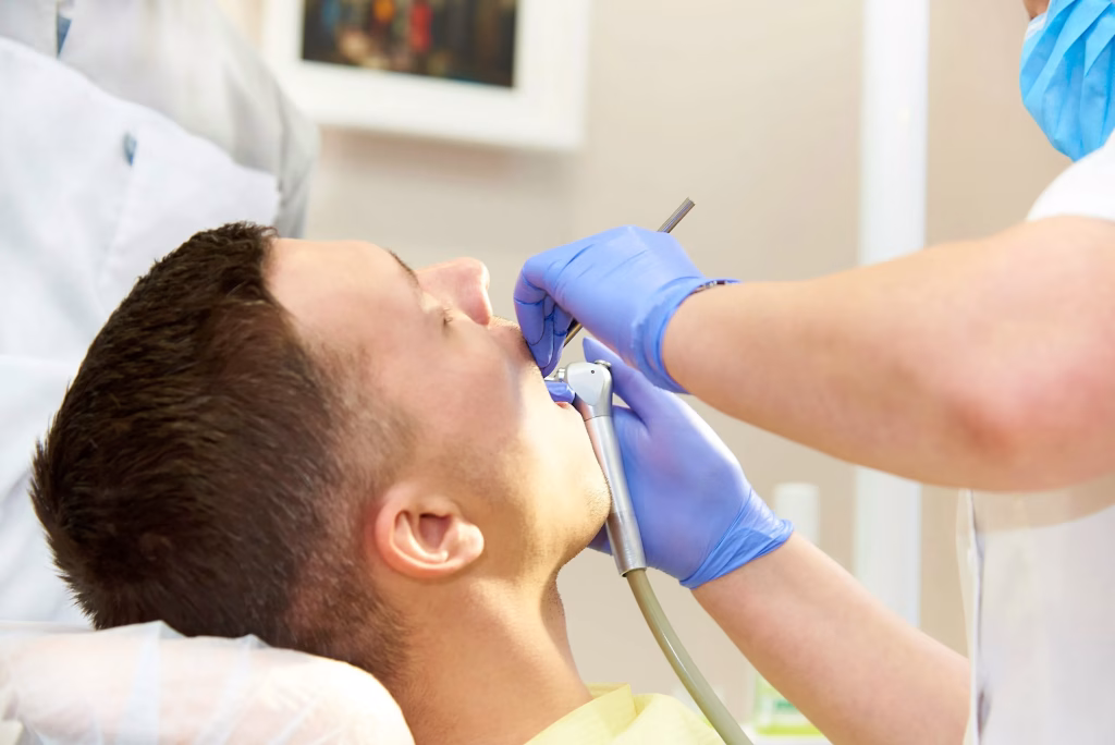 Patient receiving dental treatment in a clinic, with a dental professional using a dental tool for examination or procedure, emphasizing modern dental care and technology.